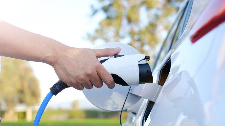 Electric car or ev is charging at station . man use the white power cable and plug on nature background. eco and clean energy concept with the mobile phone smart technology. zero gas no transmission.jpeg