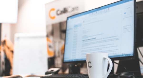A computer at a desk surrounded by branded ColliCare mug and banner