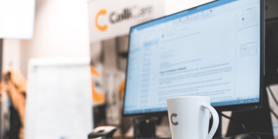 A computer at a desk surrounded by branded ColliCare mug and banner